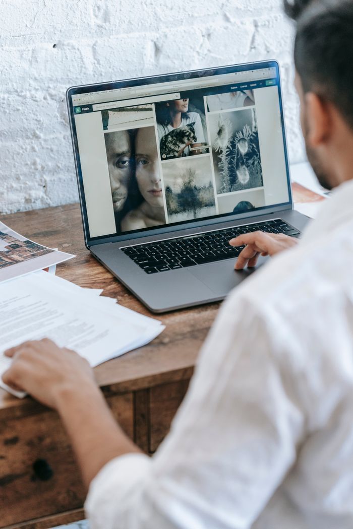 Vue de dos d’un freelance masculin anonyme, en tenue courte, assis à une table et travaillant sur un projet sur son ordinateur portable dans une pièce lumineuse en journée